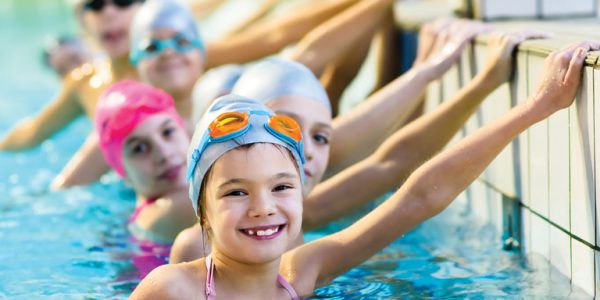 A row of smiling children holding onto the side of a swiming pool