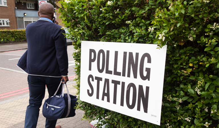 Photo shows a man walking past a polling station sign