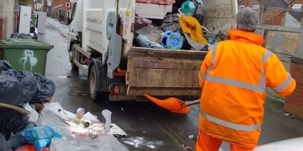 Man in high vis suit clearing dumped rubbish into a bin lorry down a tenfoot