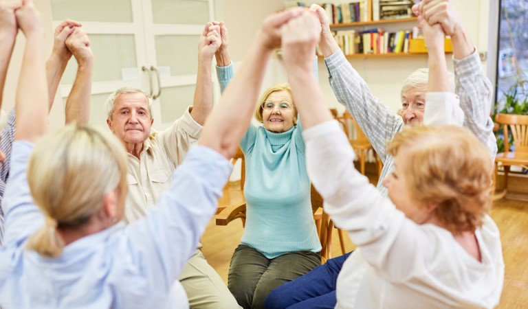 Group of older men and women doing chair based exercise 