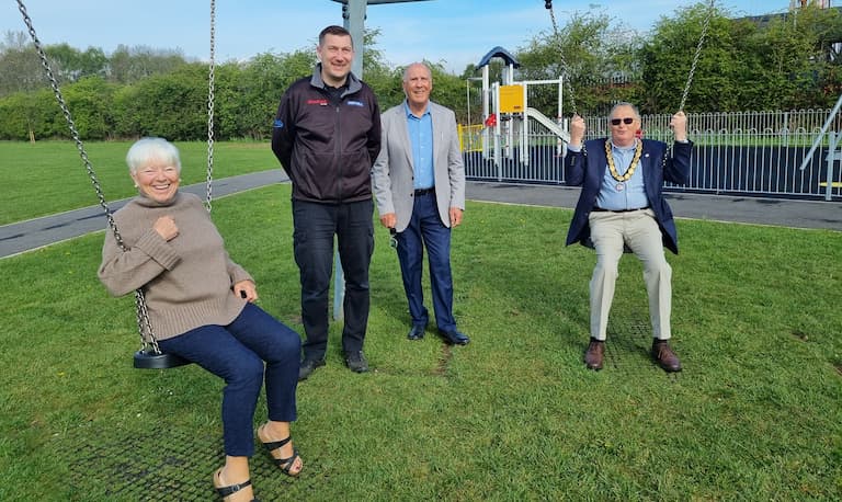 Four people, two of them on swings, at a newly refurbished park