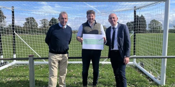 Three men holding a big cheque standing in a football goal