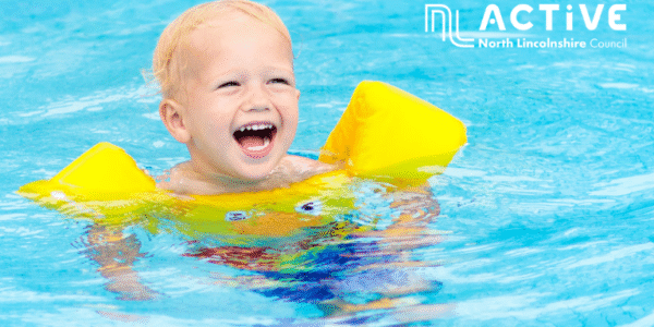 A laughing toddler in a swimming pool with yellow arm bands.
