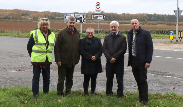 Five people standing by a crossroads junction, one in high vis