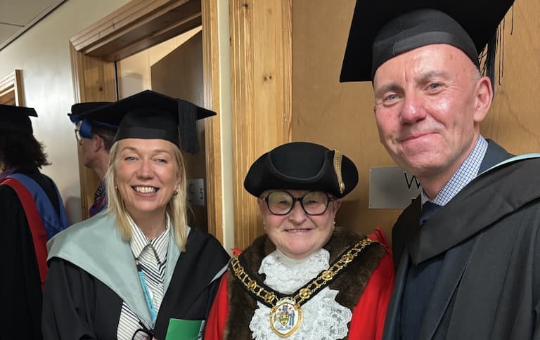 Photo of three people, two in cap and gowns and middle one in mayor's regalia