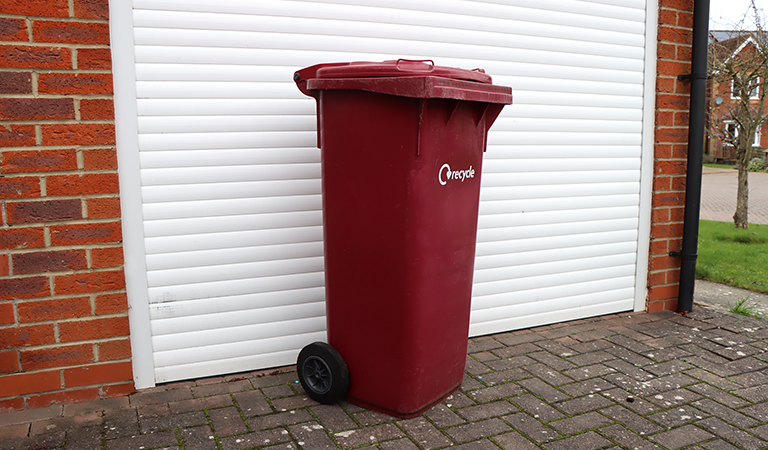Burgundy bin outside on a driveway.