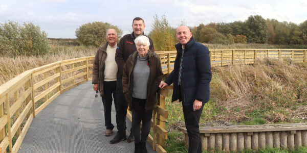 Four people standing on the boardwalk at Water's Edge surrounded by grassland