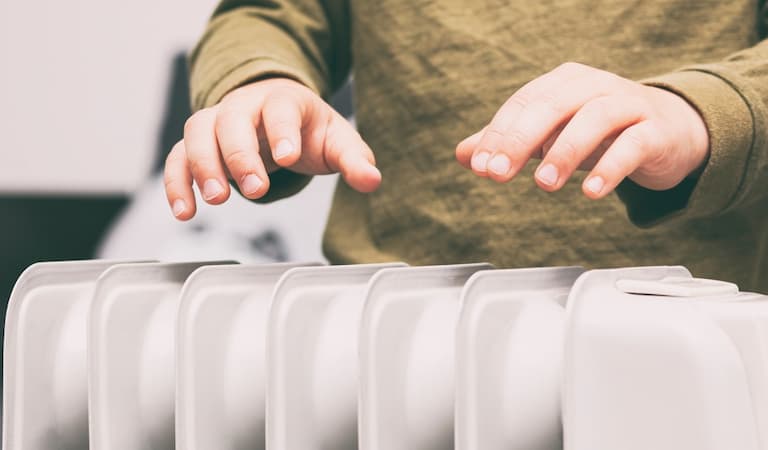Boy warms hands above the electric oil radiator