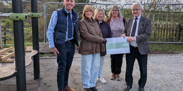 Two menadn three women holding a large cheque in a children's play area