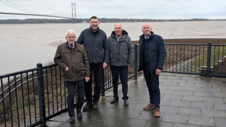 Four men standing on a walkway with the Humber Bridge in the background