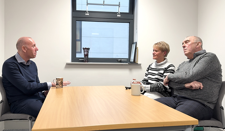 Three people sat at a long desk with a window in the centre