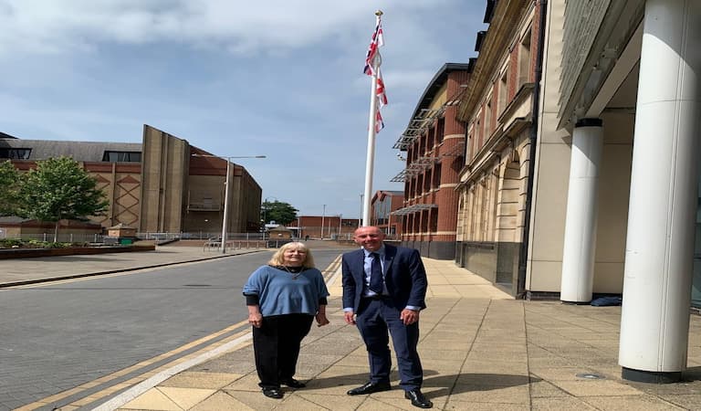 Cllr Elaine Marper and Cllr Rob Waltham stood in front of the Armed Forces Day flag that has been raised.