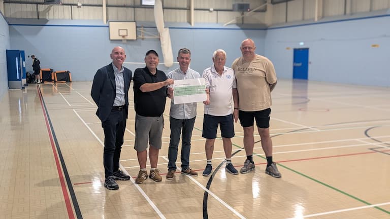 Four men in a sports hall holding a large cheque